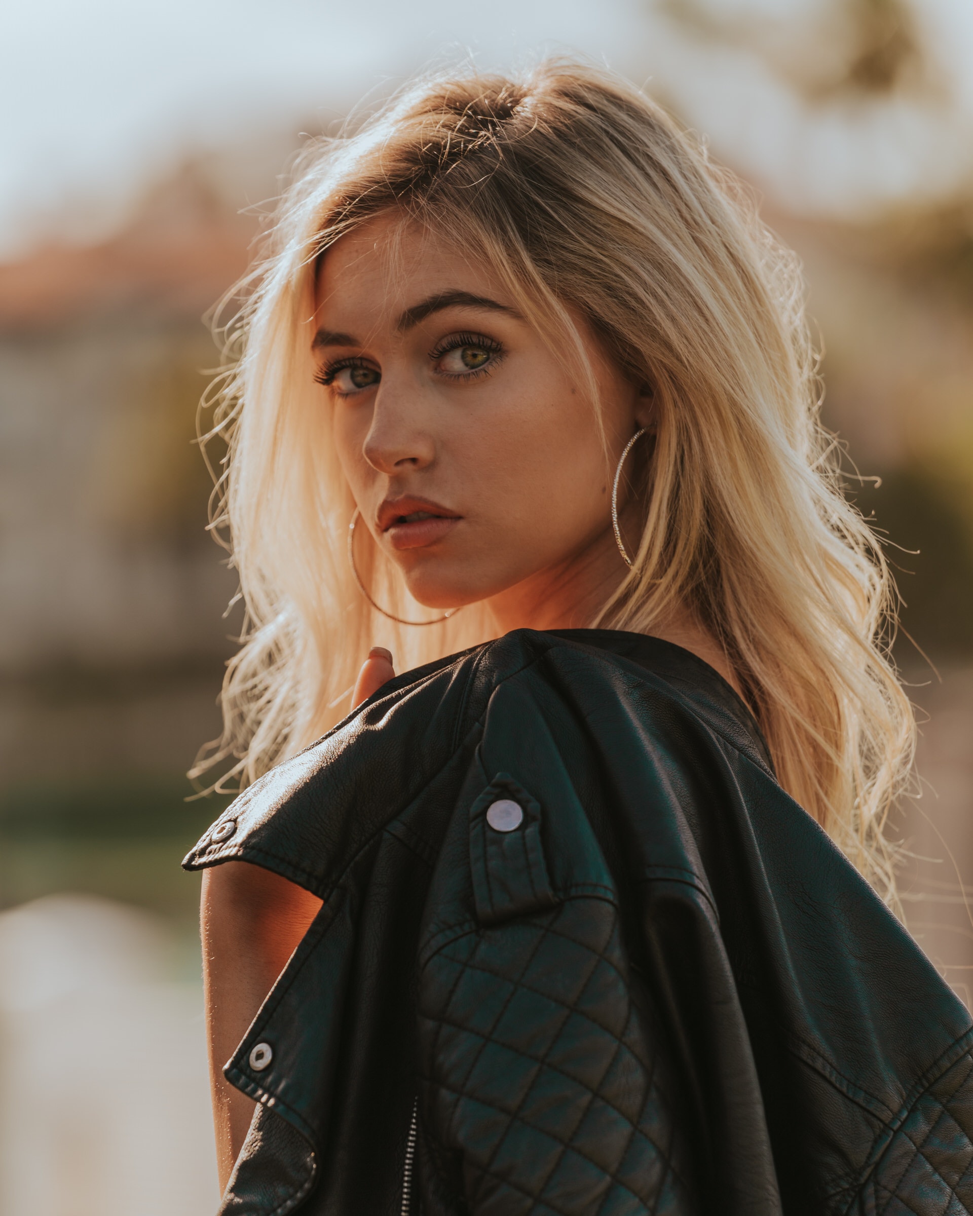 Portrait of a woman glancing over her shoulder, leather jacket draped, outdoors at golden hour.