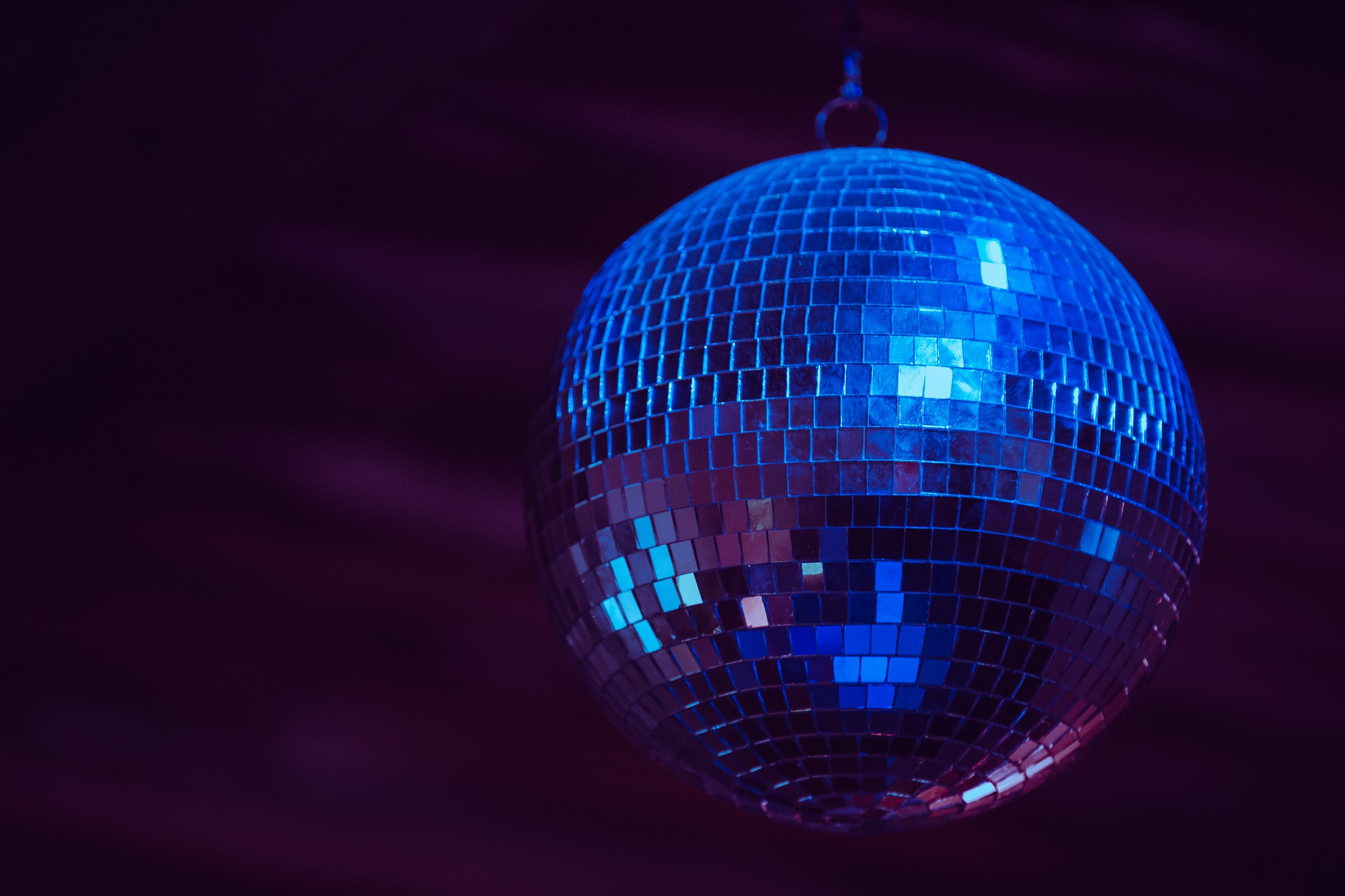 A mirrored disco ball reflects blue light against a dark purple background.