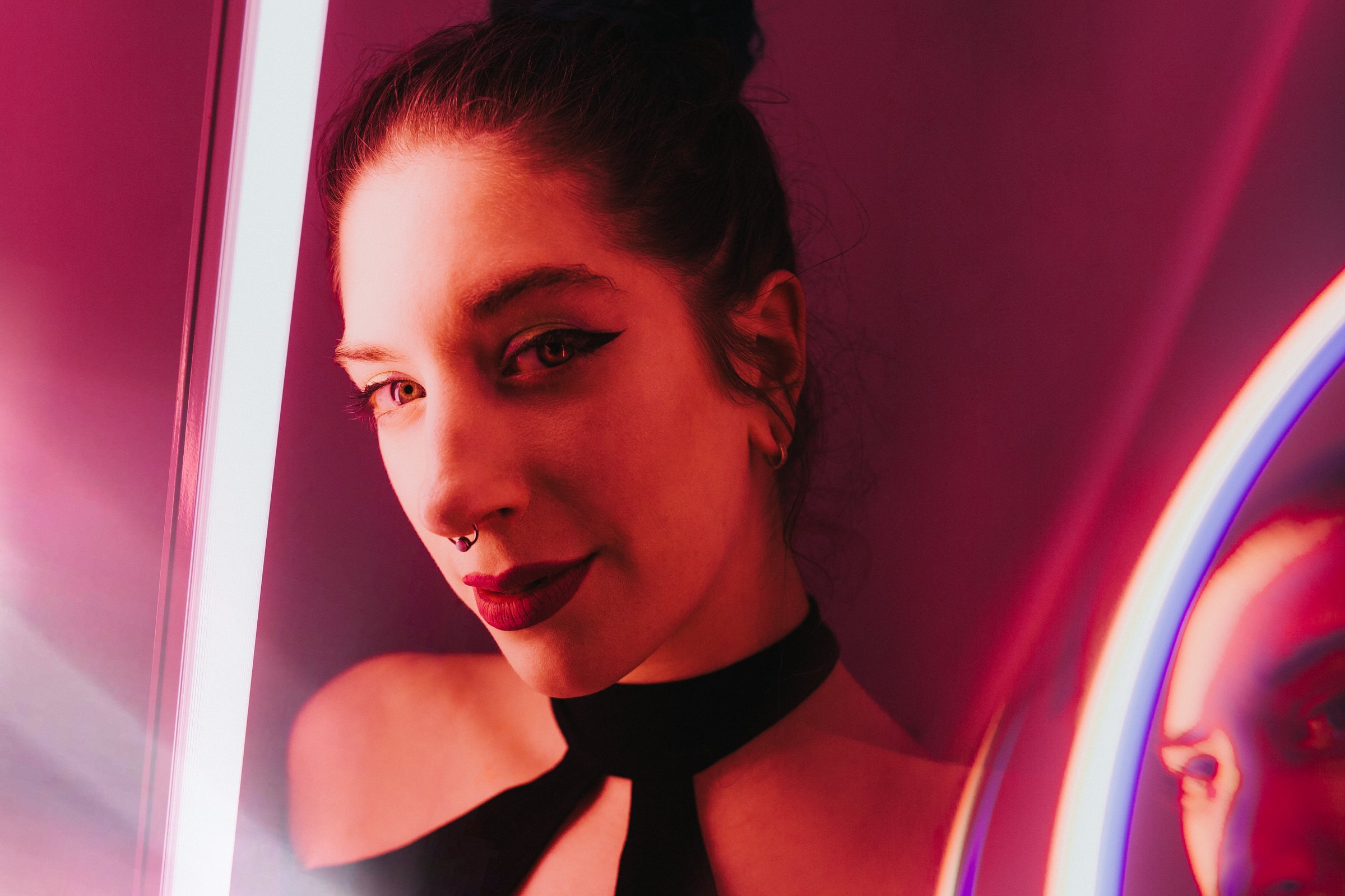 Studio portrait of a woman with septum piercing lit by pink and violet neon lights.