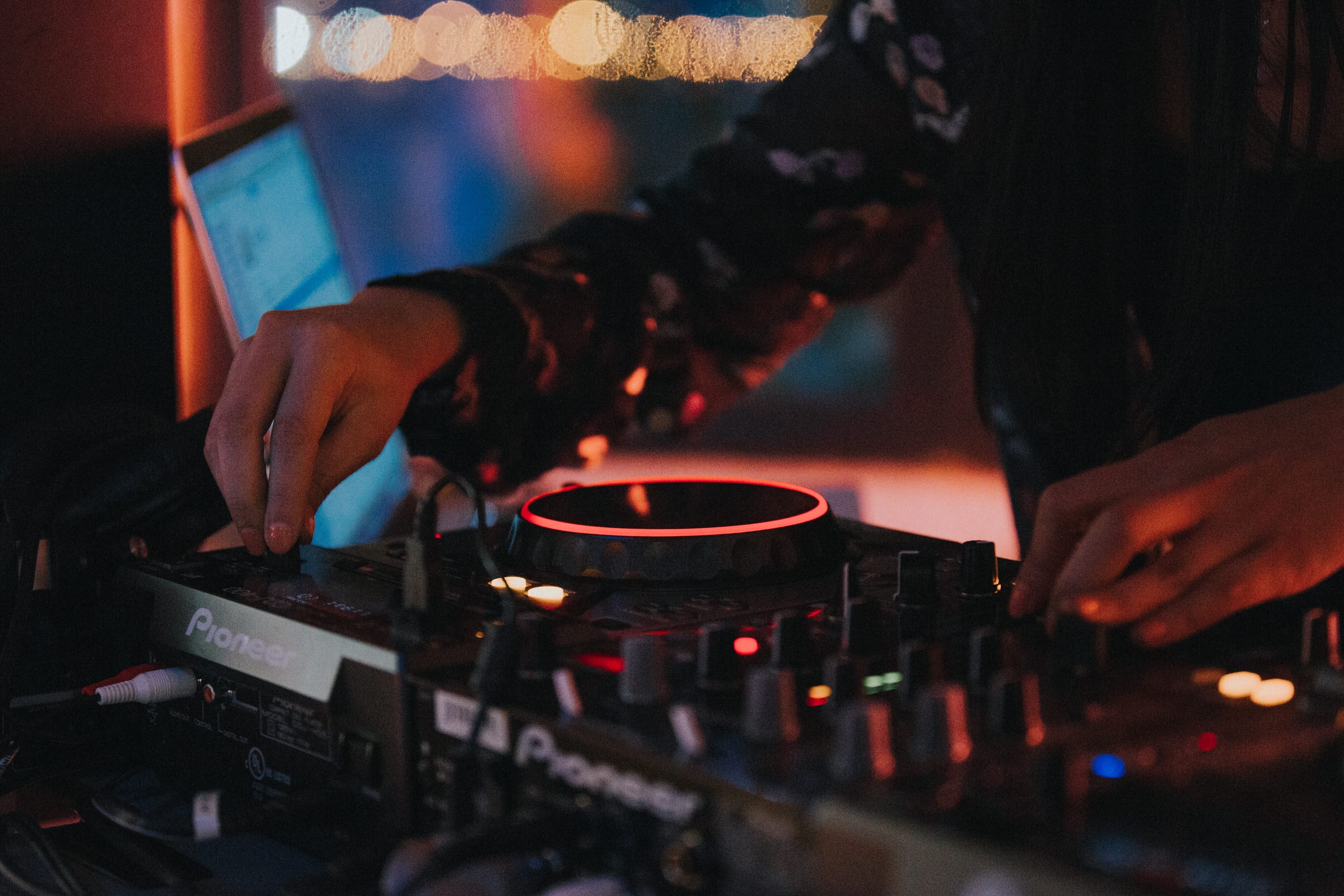 DJ adjusting knobs on a Pioneer mixer at a dimly lit nightclub event.