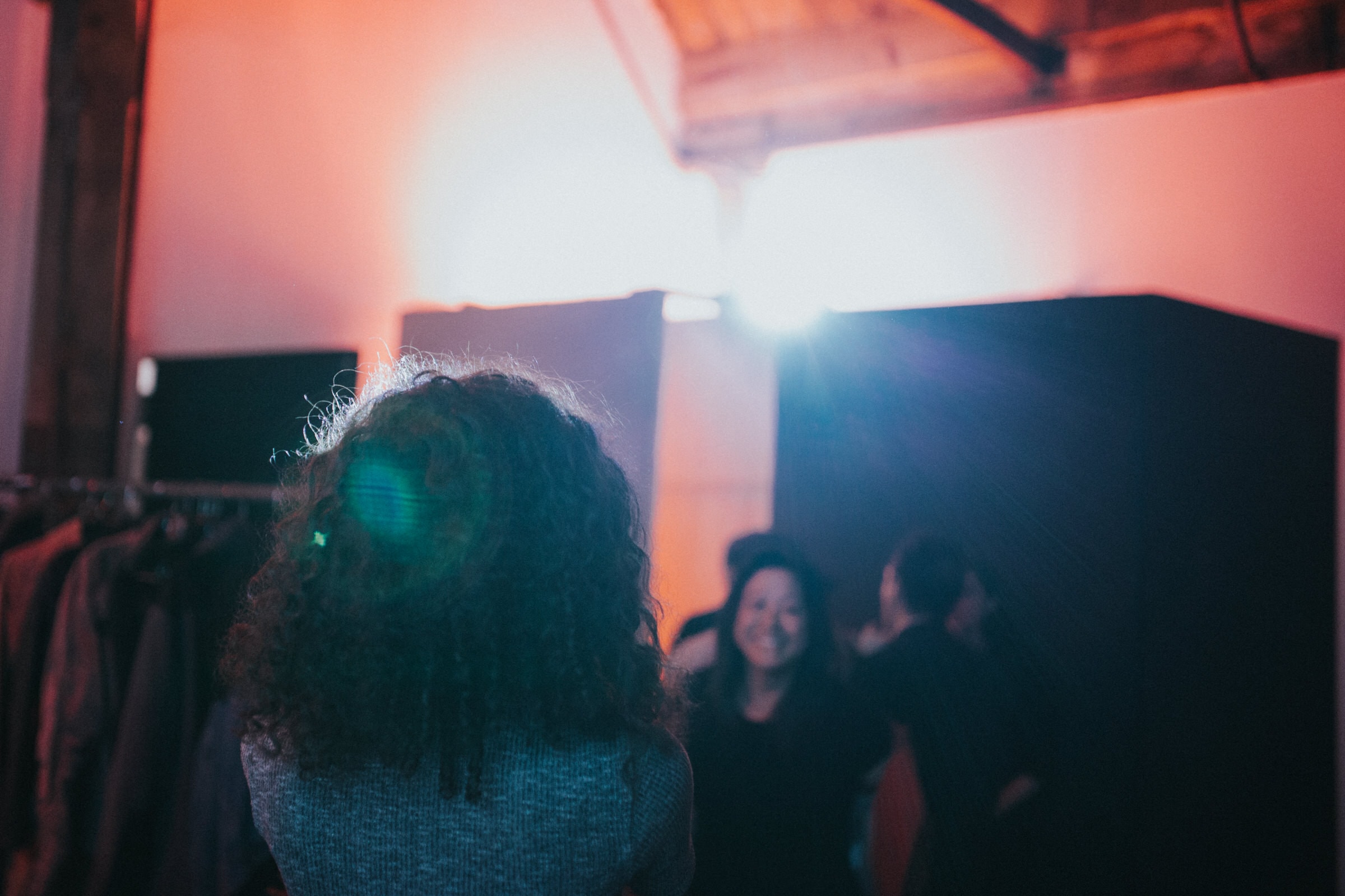 Backstage view of a photo studio with clothing racks and bright lighting during a shoot.