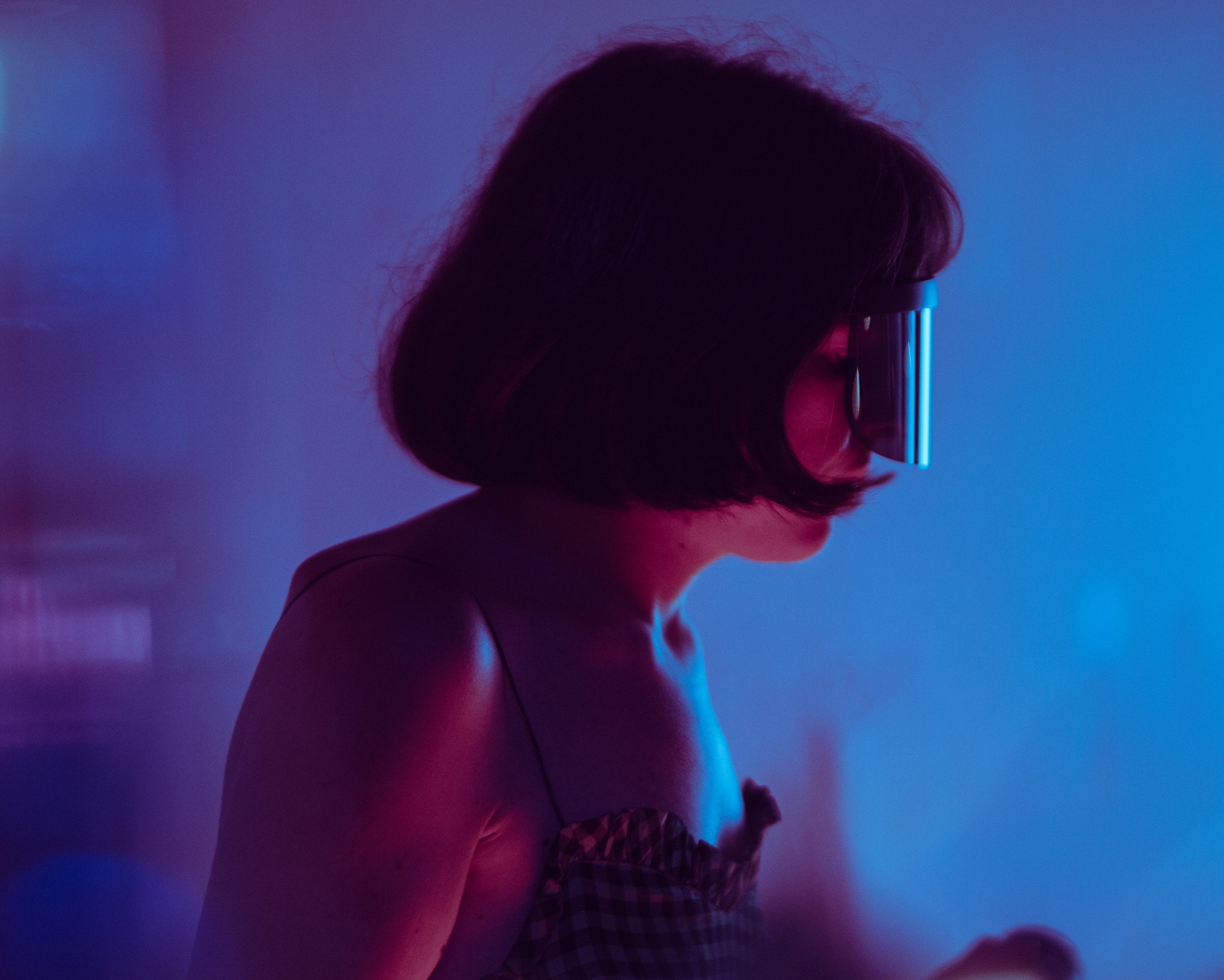 Woman in profile wears futuristic glasses under moody blue and pink nightlife lighting.