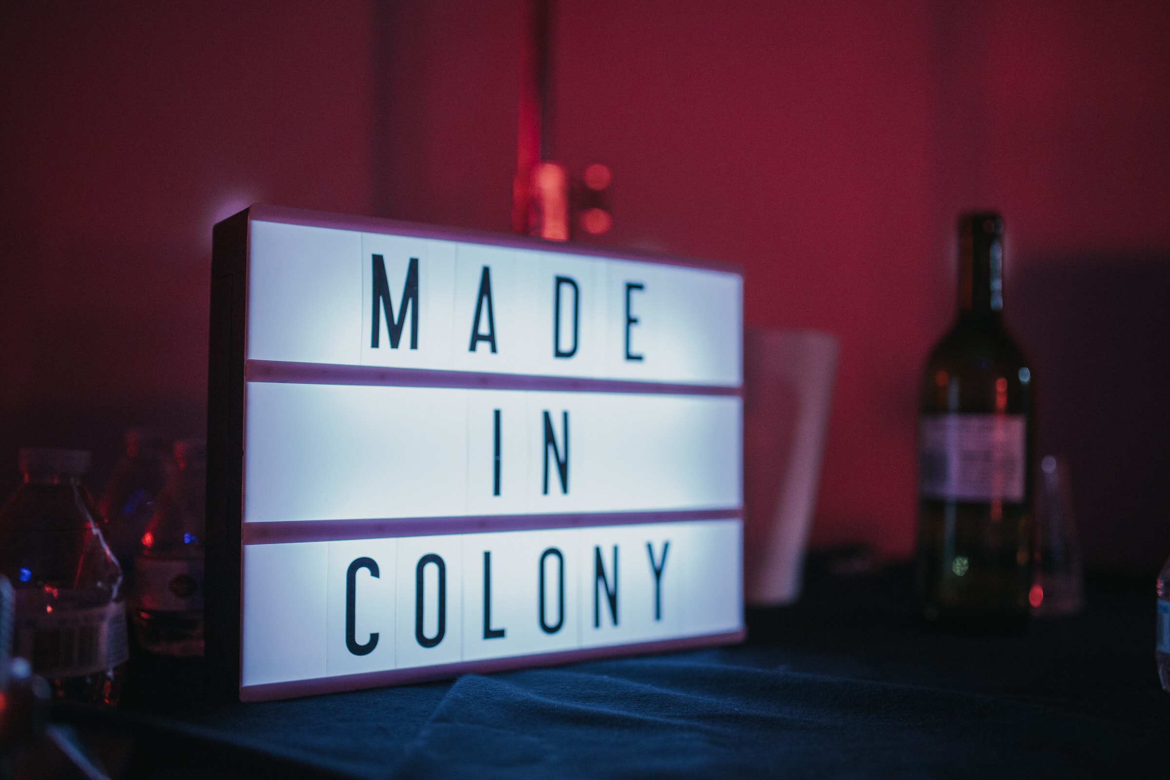 Lightbox sign reading Made In Colony on a table at a red-lit event.