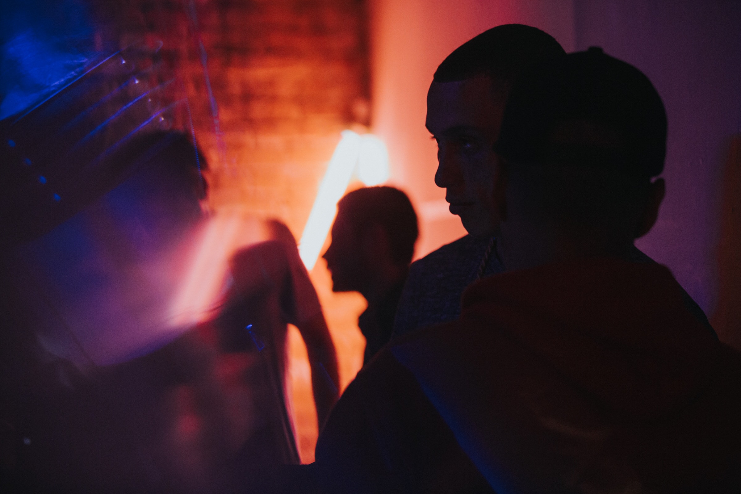 Silhouetted people at a dark event, lit by glowing orange and blue neon light.