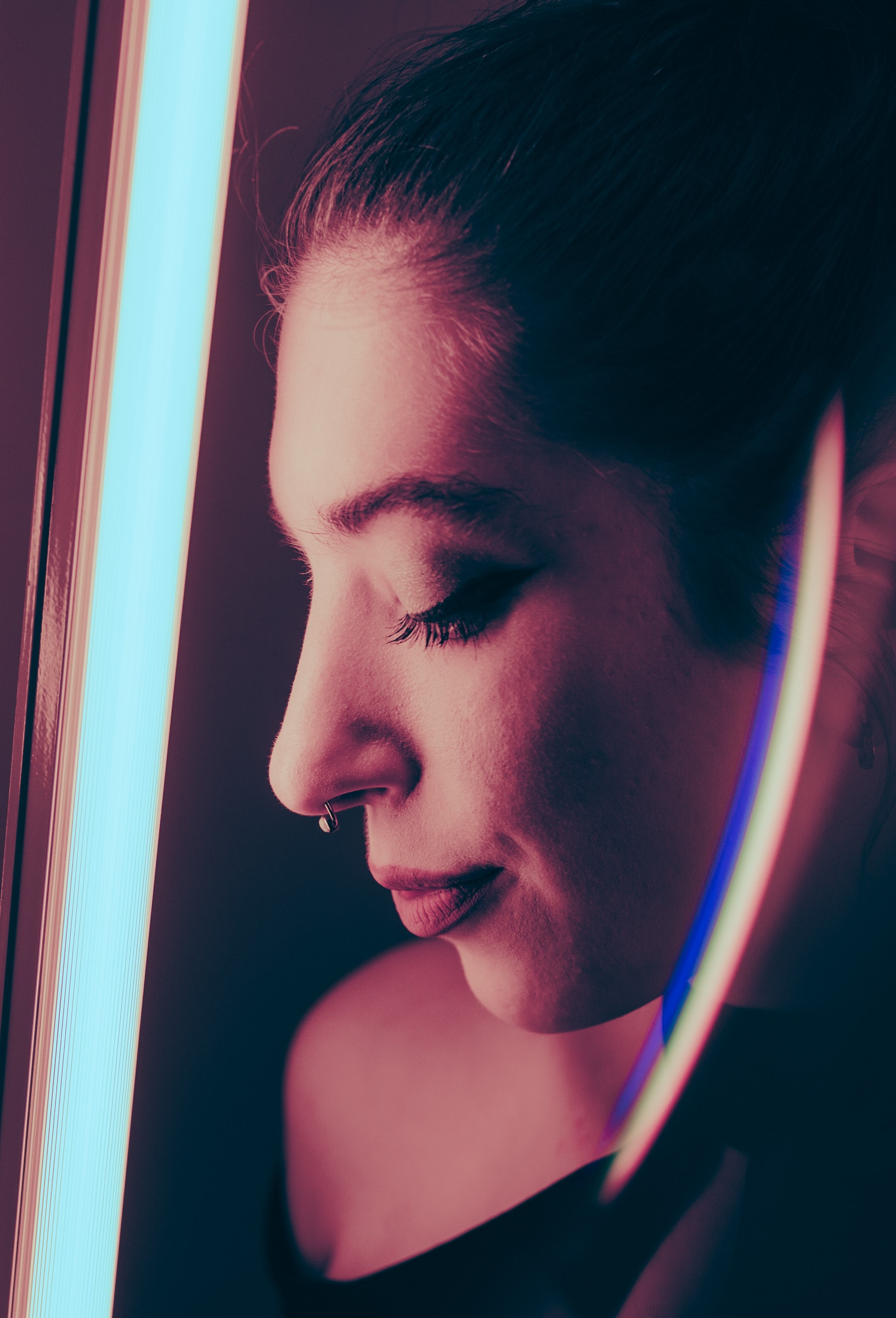 Close-up profile portrait of a woman lit by neon light with a nose ring.