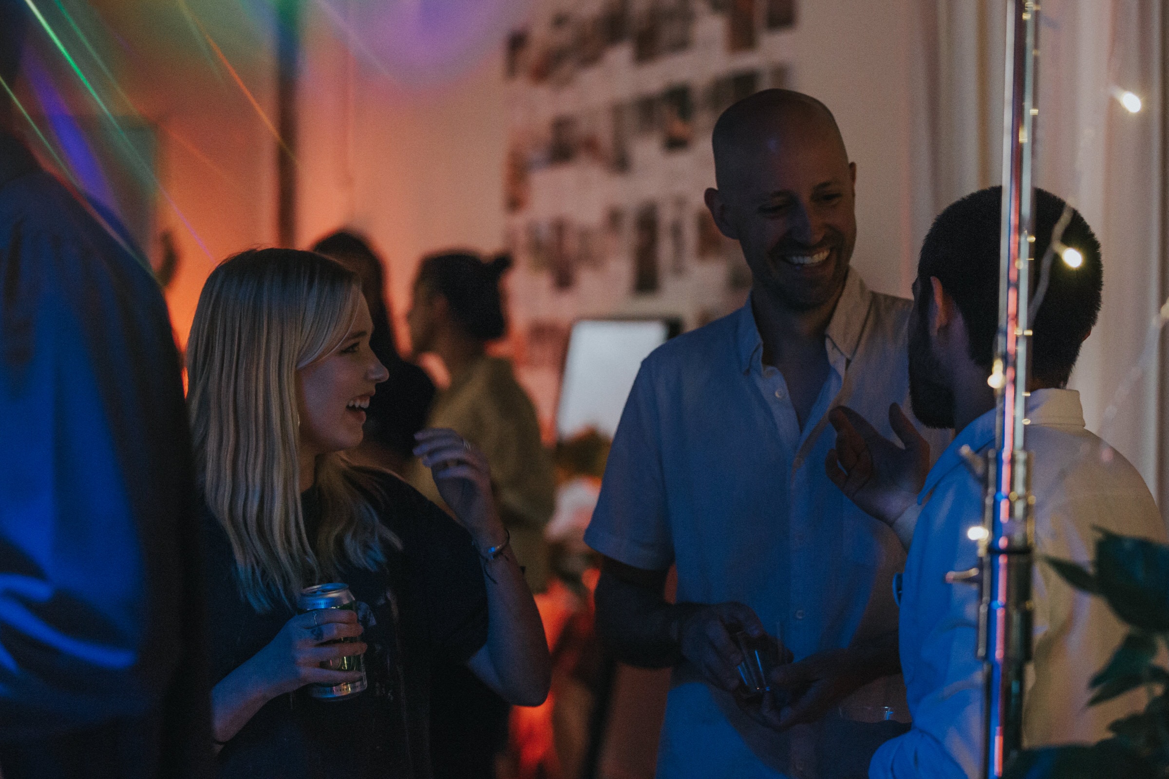 Guests laugh and chat under colorful string lights at a lively indoor evening party.