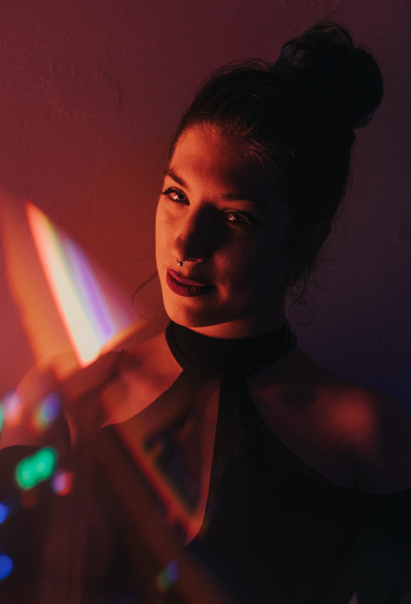 Studio portrait of a woman lit by warm red tones and colorful prism light streaks.
