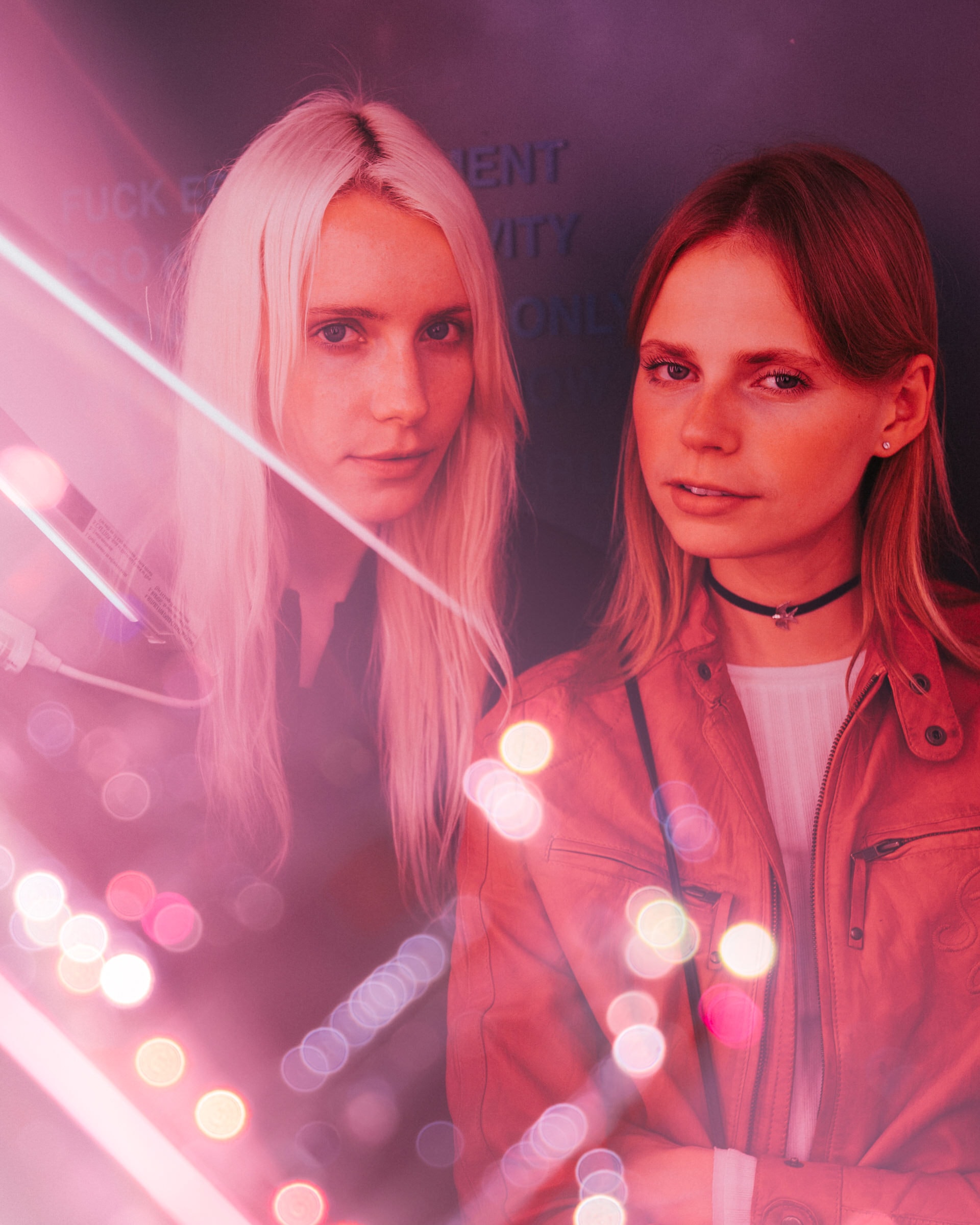 Two women lit in pink neon, bokeh lights scattered across a moody event portrait.