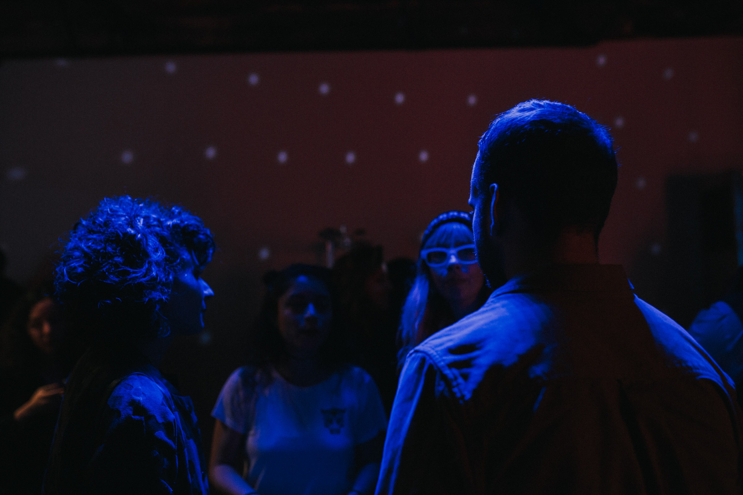 People talking under blue light at a nighttime event, projected stars on the wall.